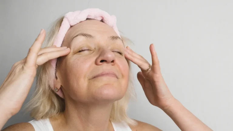 Woman in her 50s gently massaging under-eye area during skincare routine, illustrating how to look younger at 50 with healthy, rejuvenated skin.