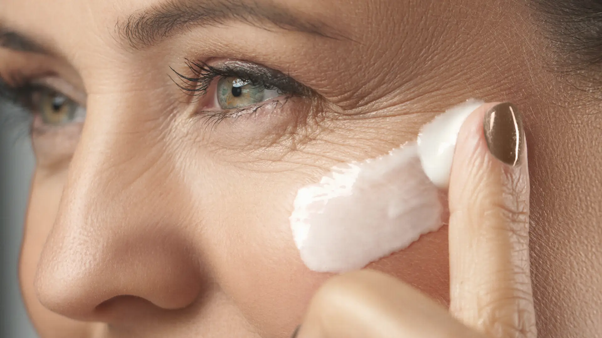 Close-up of mature woman applying eye cream to under-eye area, illustrating the question Do eye creams really fix hollows and how skincare affects under-eye appearance. BodyTonic Medspa