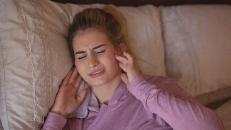 Woman lying on a pillow with her eyes shut, holding her hand against her jaw in pain