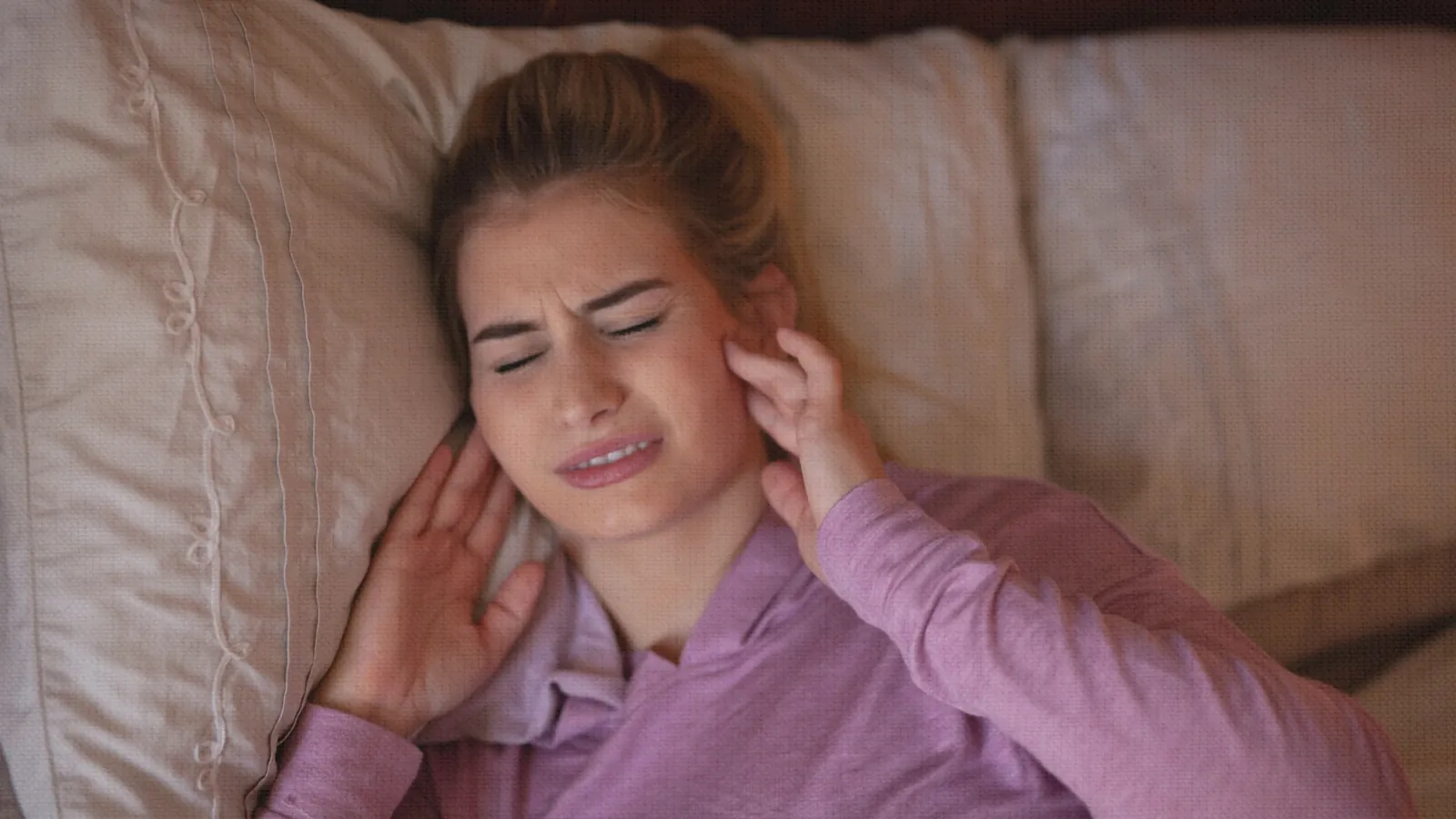Woman lying on a pillow with her eyes shut, holding her hand against her jaw in pain